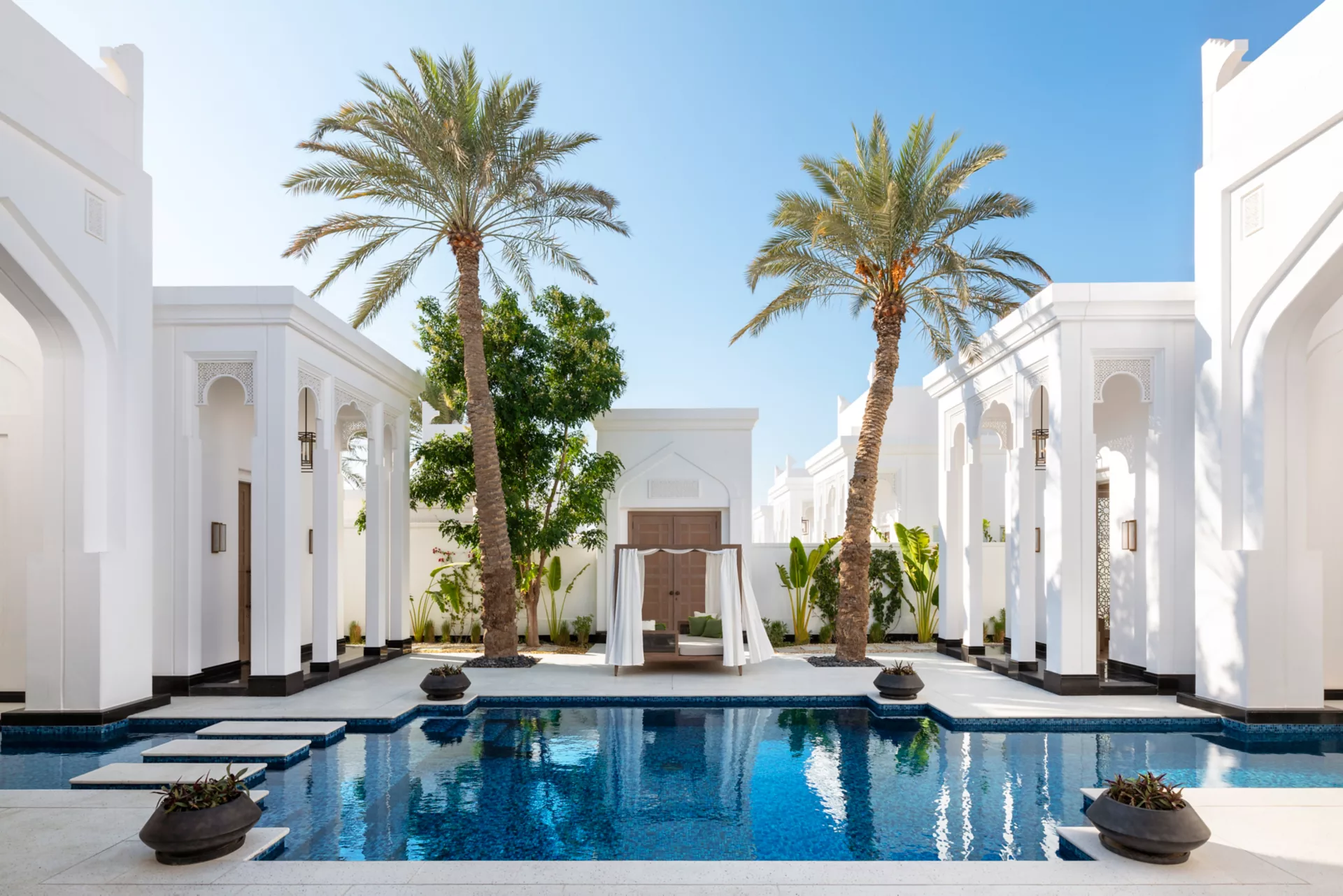 Villa pool courtyard with date palms and a canopied daybed